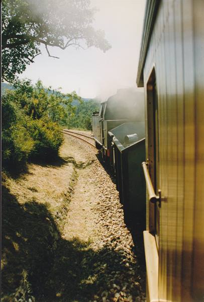 Steam locomotive among trees, white smoke, wooden train car
