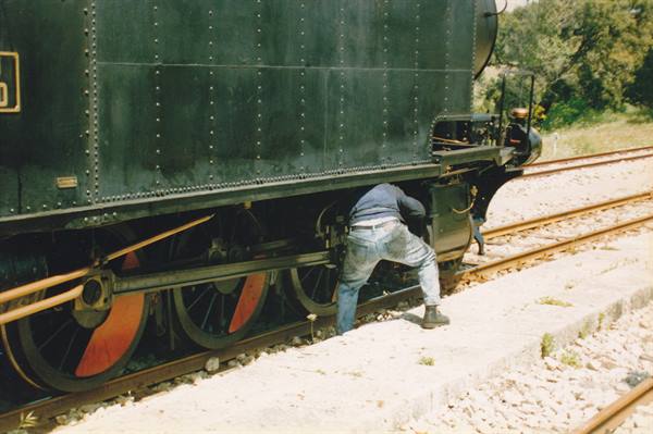 Workers repair a black steam locomotive with red wheels on the tracks