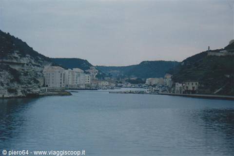 Bonifacio harbour between limestone cliffs, boats and white houses under a grey sky