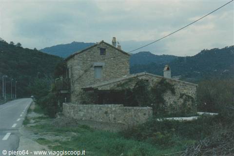 Stone farmhouse beside the road, green hills under an overcast sky