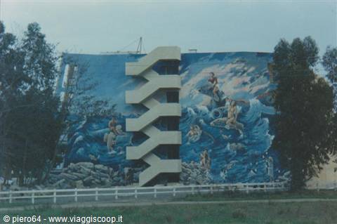 Blue sea mural on building facade with zigzag external staircase, framed by trees