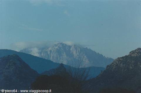 Snowy granite ridge among dark hills under pale blue sky