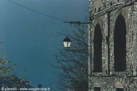 Lantern beside a stone building with arched windows, bare branches against blue sky