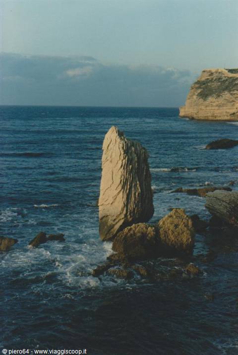 Limestone rock pinnacle among the waves, sunlit cliff on the right