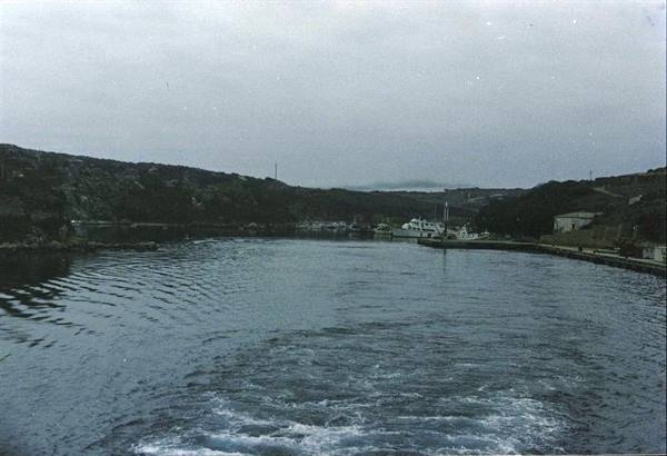 Boat wake in the harbor with quay and vessels under overcast sky