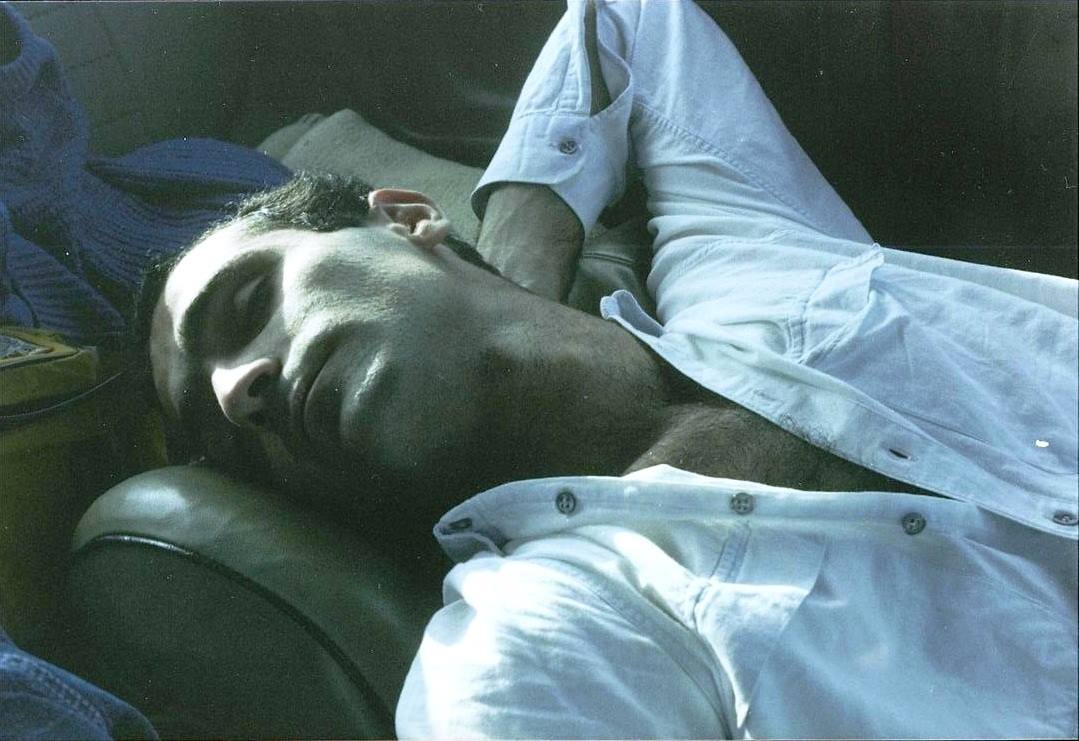 Uomo dorme su sedili scamosciati, luce solare sul viso e camicia bianca