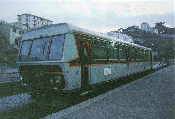 Old grey FVP railcar parked on track among buildings under cloudy sky