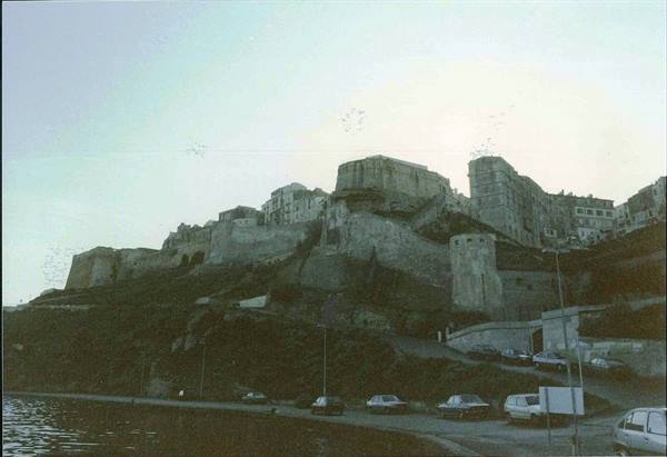 Old fortified hillside town above the sea, cars parked along the road