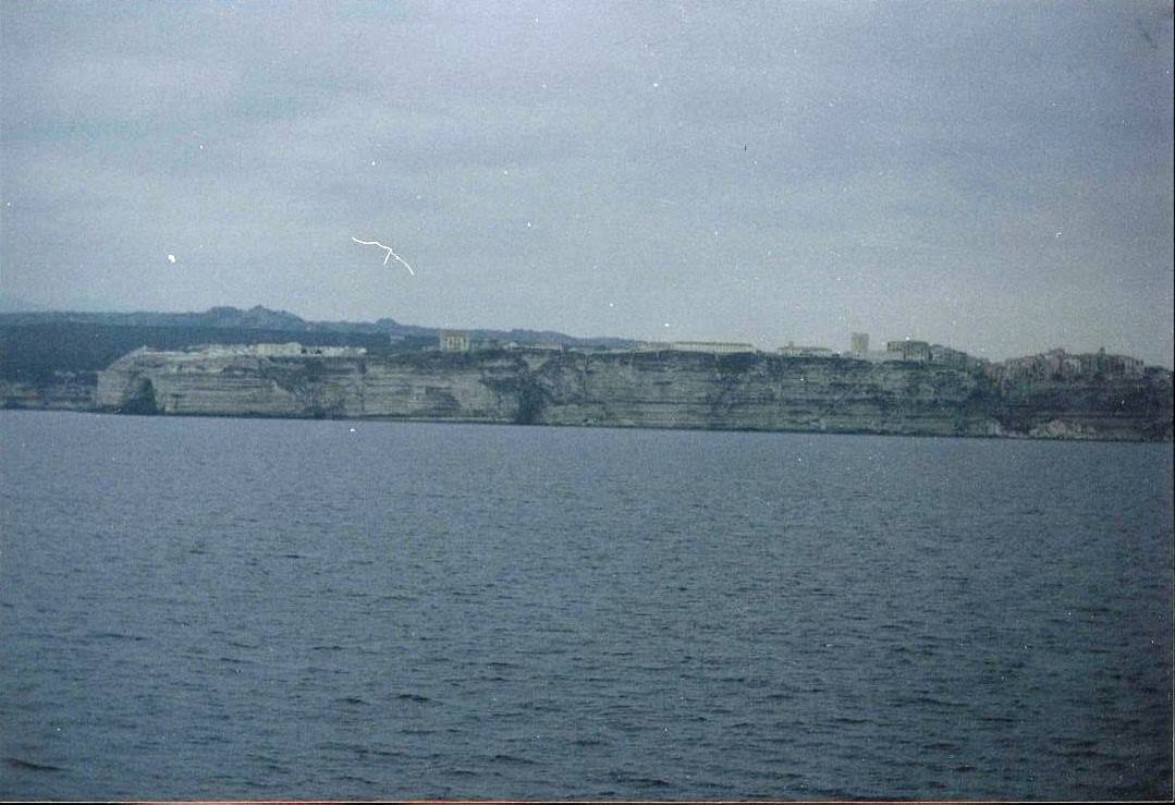Falesia calcarea con case in cima vista dal mare, cielu coperto
