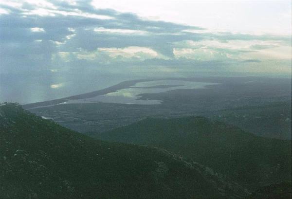 Wooded hill in foreground, lagoon and coastline under clouds with light rays
