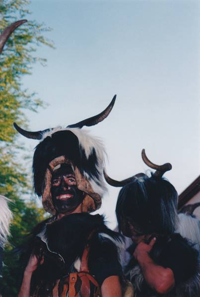Masked figures in sheepskin horned headdresses, soot-blackened faces, celebrating outdoors