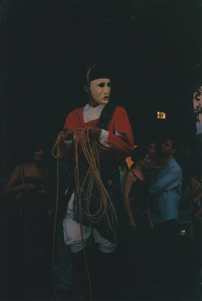 Masked performer holding rope in a nighttime street parade among the crowd