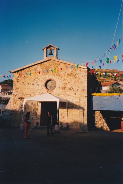 Small stone church with bell tower, colorful flags and white tent at entrance