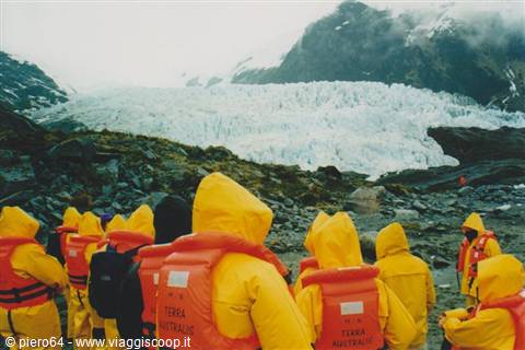 Tourists in yellow jackets and life vests watch the glacier between mountains