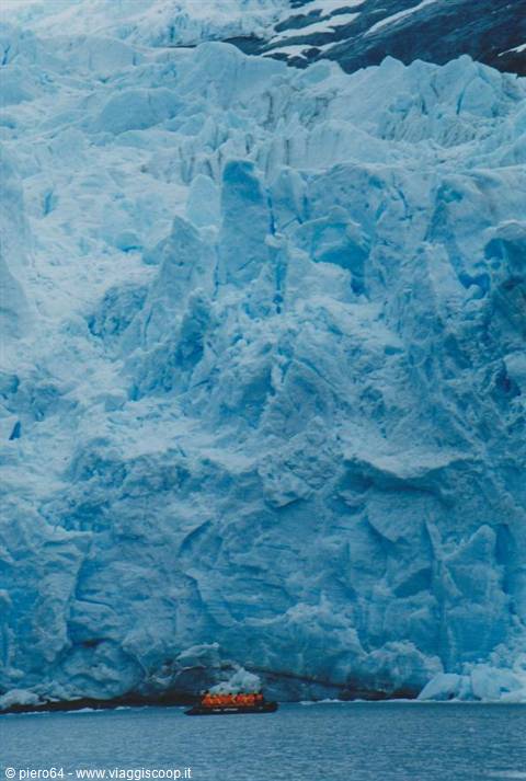Orange inflatable boat with tourists beneath a blue glacier wall