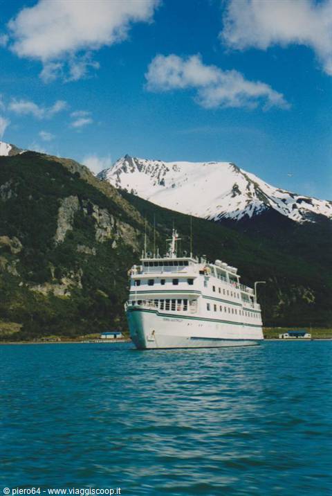 White ferry anchored in turquoise bay beneath snow-capped green mountains