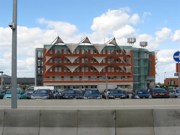 Building with white triangular canopies, parked cars, cloudy sky