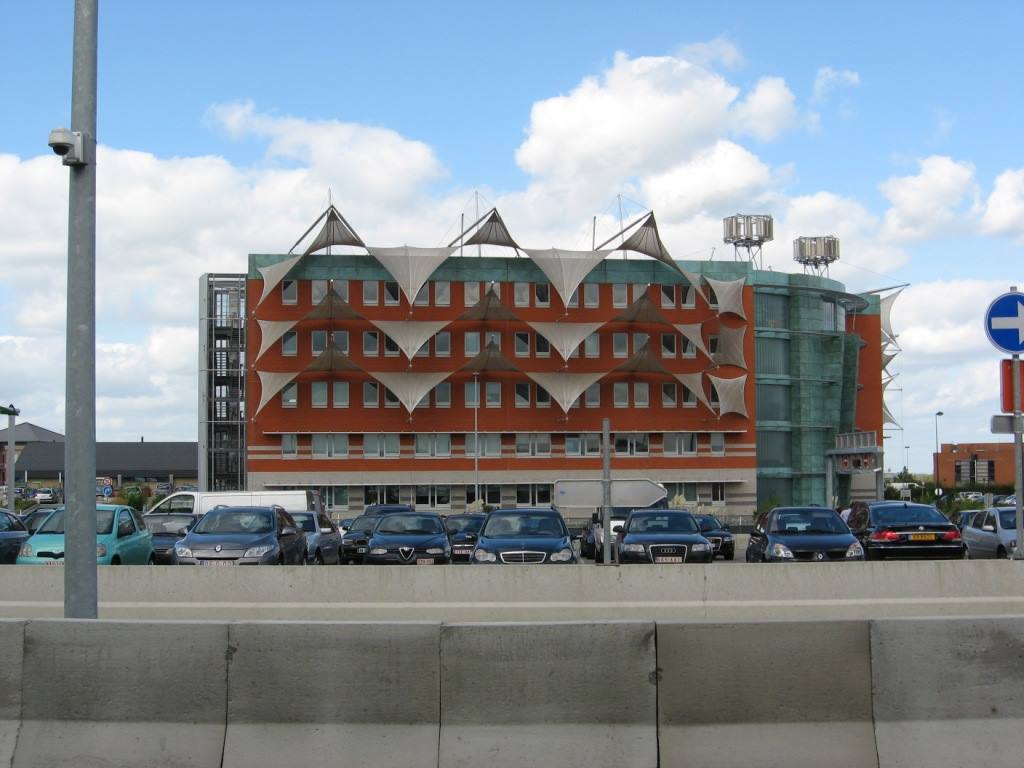 Edificio con tende triangolari bianche, parcheggio di auto, cielo nuvoloso