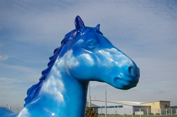 Blue and white horse statue painted like clouds, beside a hangar