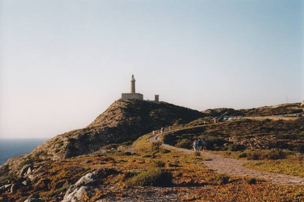 Hikers walk the path toward the lighthouse on the rocky headland
