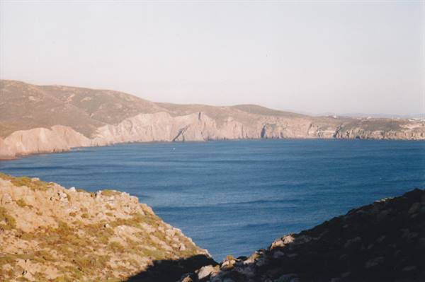 Rocky bay with arid cliffs and blue sea under pale sky