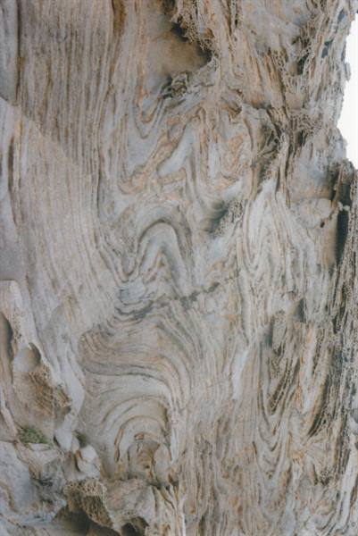 Limestone rock face with swirling folds and brown veins in daylight