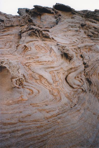 Erosion-carved rock with swirling brown layered patterns under grey sky