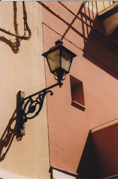 Black wrought-iron lantern on pink wall, sharp sunlight shadows
