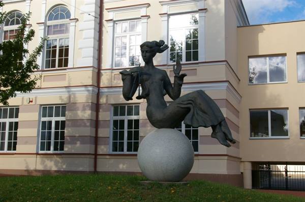 Bronze seated woman statue on granite sphere before yellow building