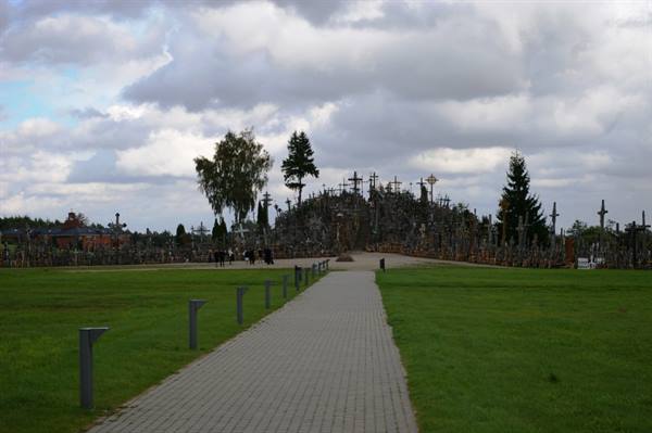 Paved walkway toward the Hill of Crosses, thousands of crosses under cloudy sky