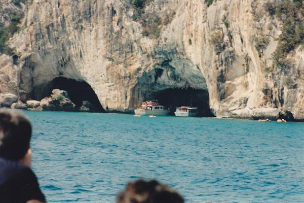 Tour boats anchored before limestone sea caves, turquoise water, Paxos