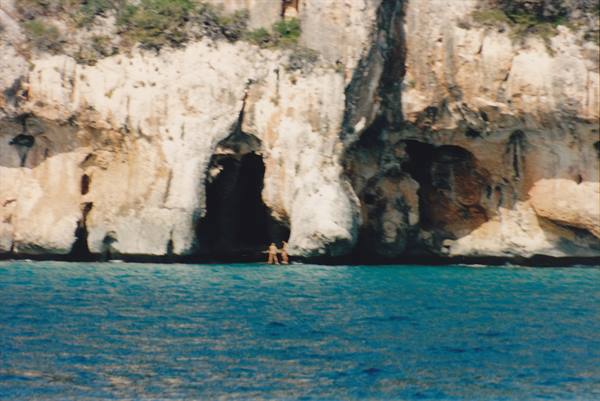 Swimmers in front of a cave in the limestone cliff by turquoise sea