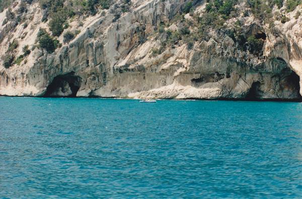 Small boat on turquoise sea beneath limestone cliffs with sea caves
