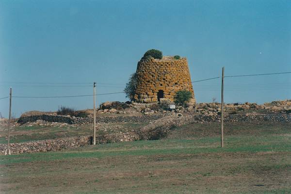 Stone nuraghe tower in countryside with dry stone walls and clear light