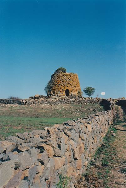 Stone nuraghe tower behind dry-stone walls under clear blue sky