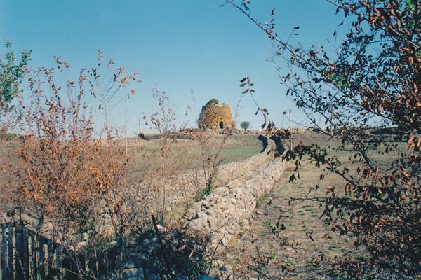 Stone nuraghe among dry hills, bare bushes and walls, blue sky
