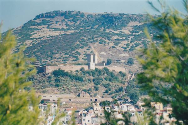 Medieval fortress with tower on the hill, white houses among pines in foreground