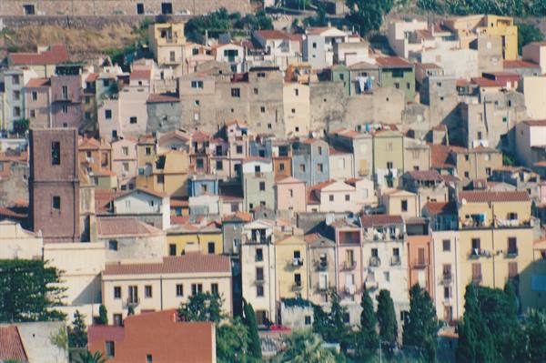 Colorful houses stacked on a hillside, tiled roofs and a brick bell tower
