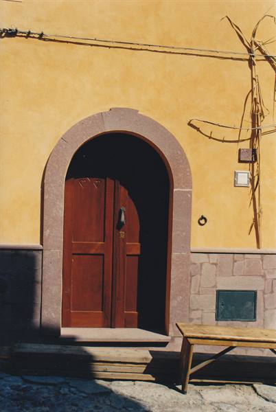 Red wooden door under stone arch on yellow wall, wooden bench