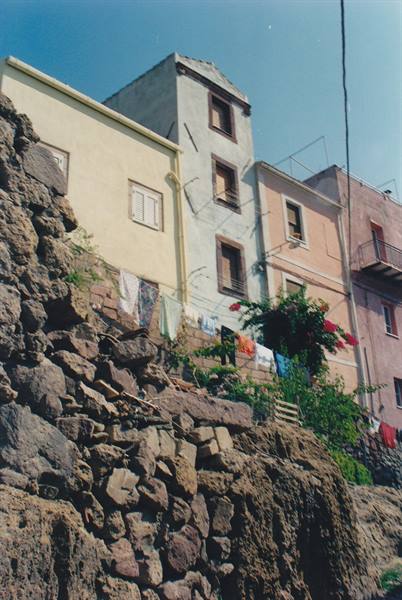 Colored houses on volcanic rock, laundry hanging between buildings, red flowers