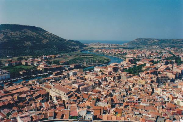 Red rooftops of Bosa crossed by the Temo river, hills and sea beyond