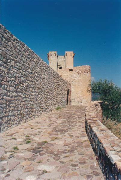 Stone-paved path between castle walls and tower under a blue sky