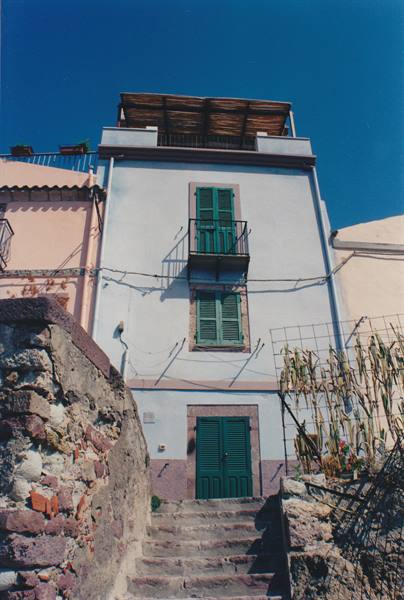 White house with green shutters and stone steps under a blue sky