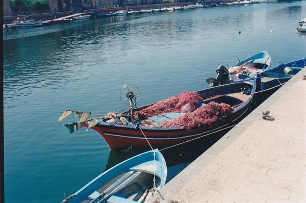 Red fishing boat with pink nets moored at the quay beside other boats
