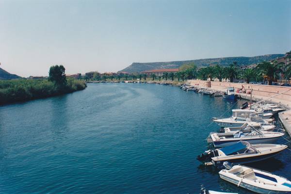 Motorboats moored along the Bosa river, palm trees and houses on the waterfront