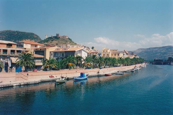 Boats moored along the Temo river in Bosa, palm trees and colorful houses