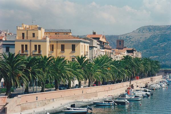 Waterfront lined with palm trees, yellow buildings and moored boats in Bosa