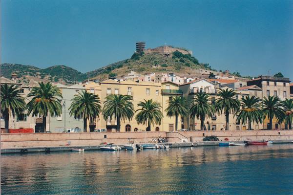 Palms and colorful houses along the Temo river in Bosa, castle on the hill