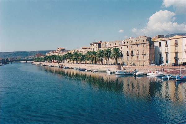 Boats moored along the Temo river in Bosa, buildings and palms reflected in the water