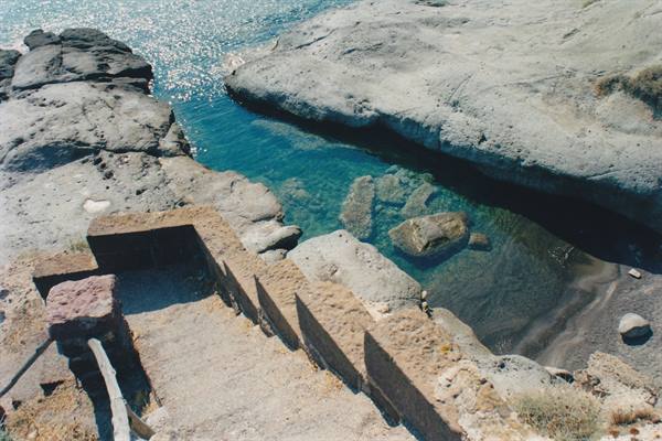 Stone stairs descending to natural pool with turquoise water among volcanic rocks
